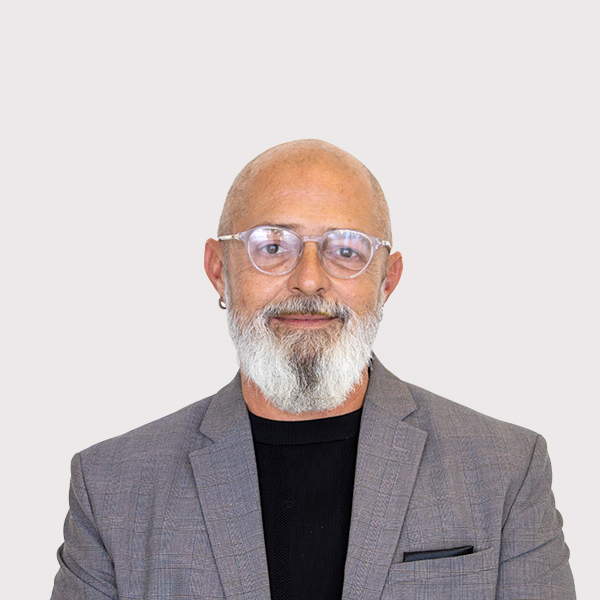 Professional headshot of a man with a bald head and beard, wearing glasses and a gray blazer.